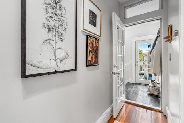 hallway featuring wood finished floors, baseboards, and french doors