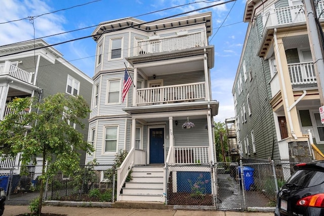 townhome / multi-family property with a balcony, a gate, a fenced front yard, and covered porch