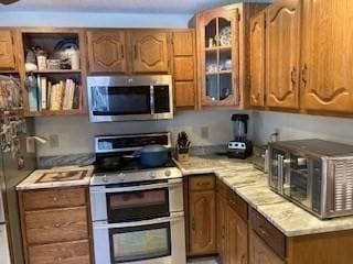 kitchen with a toaster, brown cabinetry, glass insert cabinets, appliances with stainless steel finishes, and light countertops