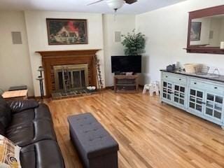 living area featuring a fireplace with raised hearth, ceiling fan, and wood finished floors