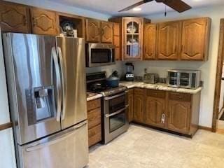 kitchen with stainless steel appliances, light countertops, glass insert cabinets, and brown cabinets