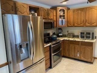 kitchen featuring stainless steel appliances, brown cabinetry, light countertops, and glass insert cabinets