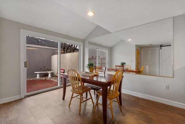 dining space with a barn door, lofted ceiling, and light hardwood / wood-style flooring