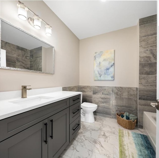 full bath featuring vanity, a wainscoted wall, toilet, marble finish floor, and tile walls