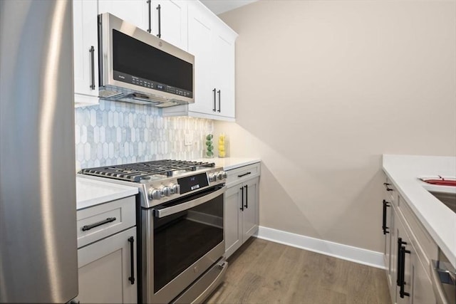 kitchen featuring appliances with stainless steel finishes, wood finished floors, light countertops, decorative backsplash, and baseboards