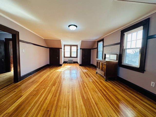 unfurnished living room featuring radiator heating unit, light wood-type flooring, crown molding, and a healthy amount of sunlight