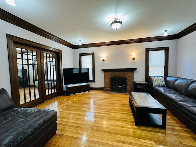 living room with french doors, light wood-type flooring, ornamental molding, and a brick fireplace