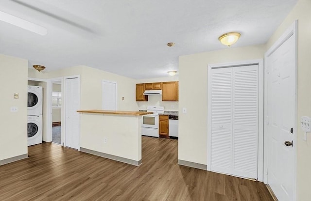 kitchen with white appliances, stacked washer and clothes dryer, under cabinet range hood, dark wood finished floors, and light countertops