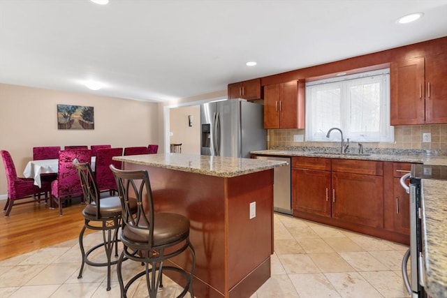 kitchen featuring sink, decorative backsplash, a kitchen island, light stone counters, and stainless steel appliances