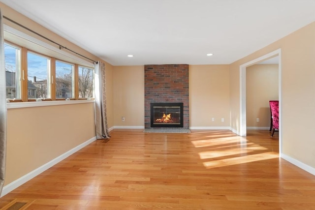 unfurnished living room featuring light hardwood / wood-style flooring and a brick fireplace