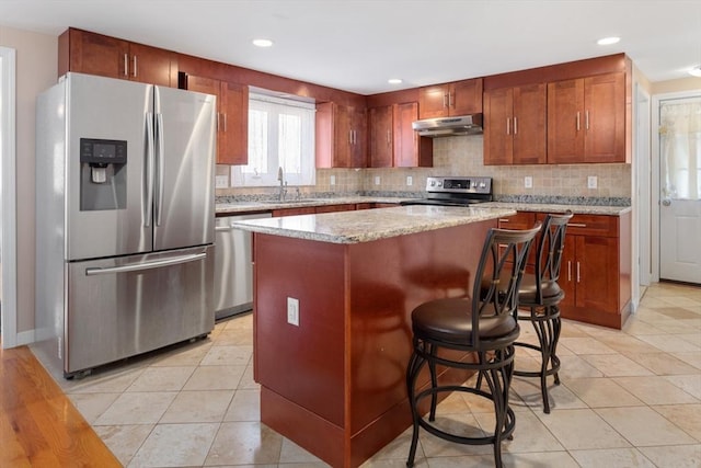 kitchen featuring light stone countertops, a center island, sink, stainless steel appliances, and a kitchen bar