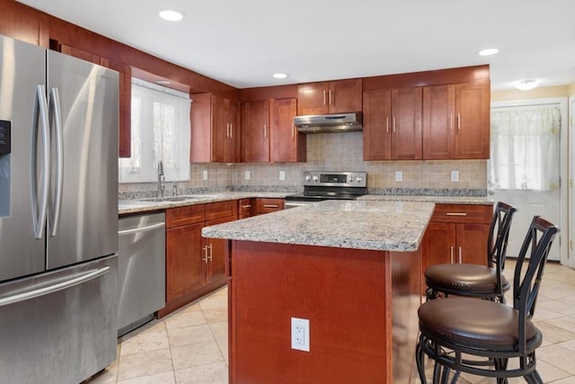 kitchen with a kitchen bar, light stone countertops, stainless steel appliances, sink, and a kitchen island