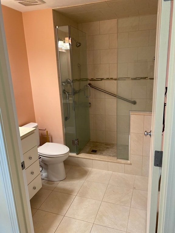 bathroom with a shower with door, toilet, vanity, and tile patterned flooring