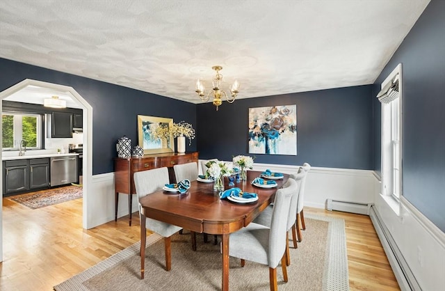 3 Penni Ln, Andover, MA 01810 - dining room featuring a chandelier, light wood-style floors, a baseboard heating unit, arched walkways, and wainscoting