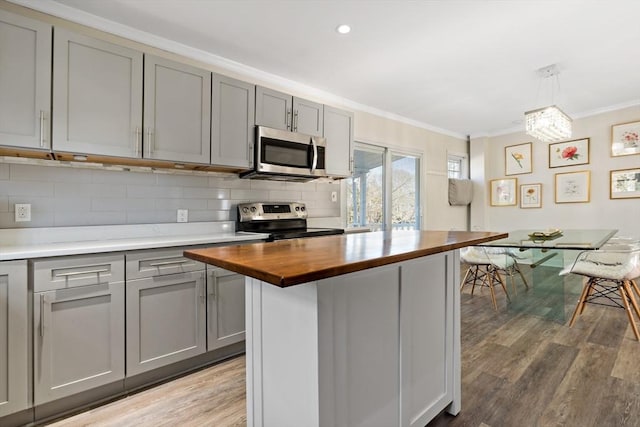 kitchen with pendant lighting, stainless steel appliances, a kitchen island, gray cabinets, and butcher block countertops