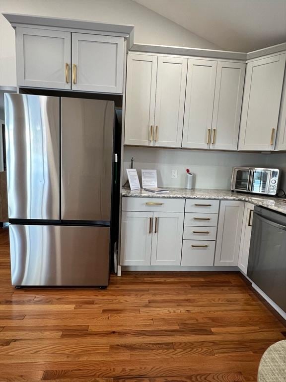 kitchen featuring light wood finished floors, a toaster, lofted ceiling, light stone counters, and stainless steel appliances