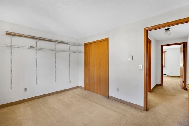 unfurnished bedroom with a closet, baseboard heating, light colored carpet, and baseboards