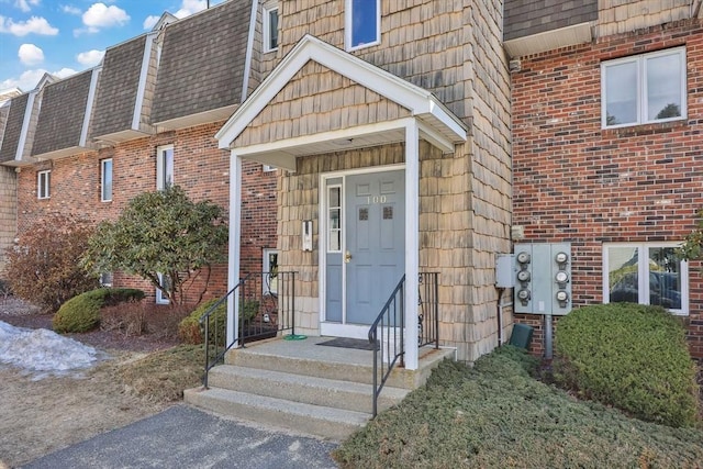 property entrance featuring mansard roof, a shingled roof, and brick siding