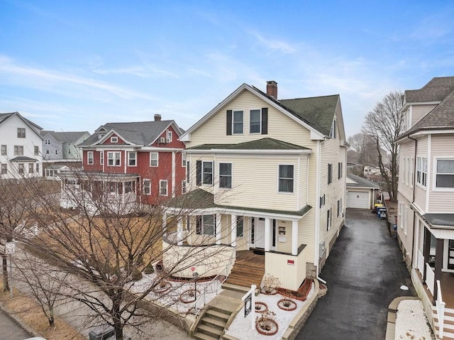 view of front of home featuring aphalt driveway, a detached garage, a chimney, a residential view, and an outdoor structure