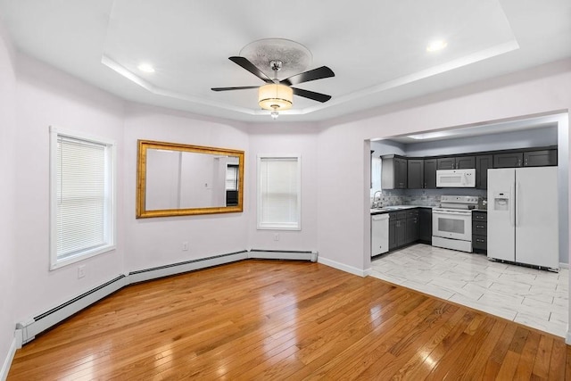 kitchen featuring light wood-type flooring, a tray ceiling, white appliances, and a sink