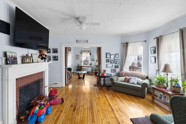 living area featuring ceiling fan, crown molding, a fireplace, and light wood-style floors