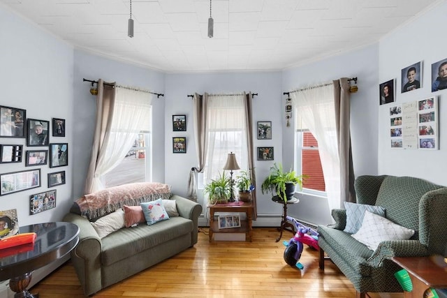 sitting room featuring light wood-type flooring, a healthy amount of sunlight, a baseboard heating unit, and crown molding