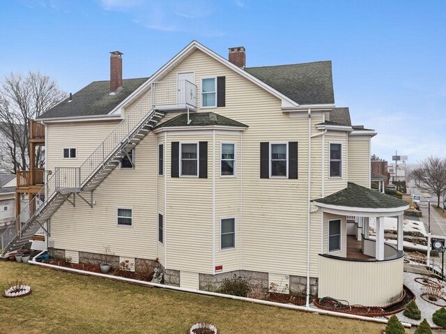 rear view of house with stairs, a yard, a shingled roof, and a chimney