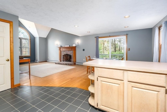 kitchen with lofted ceiling, light brown cabinetry, a healthy amount of sunlight, and a fireplace