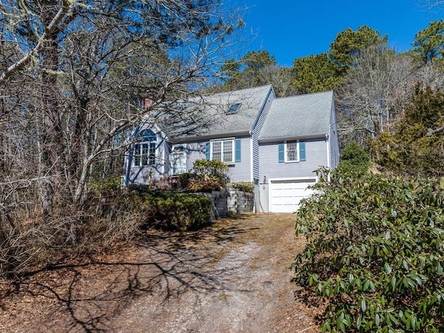 view of front facade with a garage, roof with shingles, and dirt driveway
