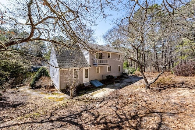 rear view of property with a balcony, a shingled roof, and a chimney