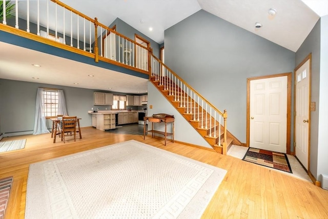 entryway with light wood finished floors, baseboards, high vaulted ceiling, and stairway