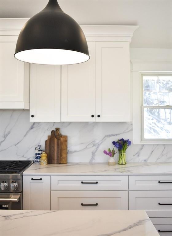 kitchen featuring backsplash, stainless steel stove, light stone countertops, and white cabinets