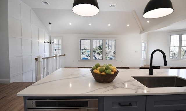 kitchen with vaulted ceiling, pendant lighting, an island with sink, sink, and light stone countertops