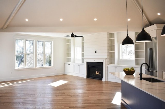 living room featuring sink, built in features, ceiling fan, a fireplace, and hardwood / wood-style floors