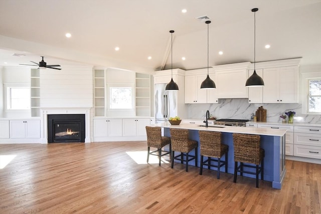 kitchen with a breakfast bar, white cabinetry, lofted ceiling, hanging light fixtures, and a center island with sink