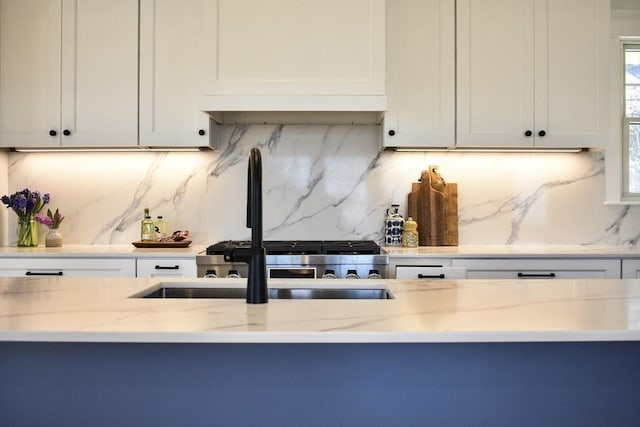 kitchen with light stone countertops, range, white cabinets, and decorative backsplash