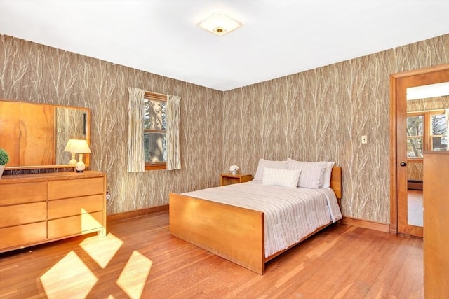 bedroom with a baseboard heating unit, multiple windows, baseboards, and wood finished floors