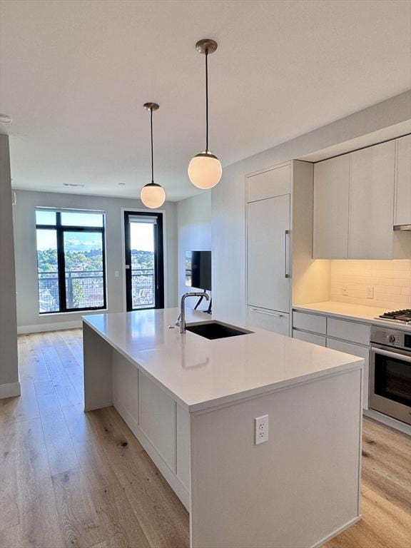191 Washington St Unit 708, Boston, MA 02135 - kitchen featuring appliances with stainless steel finishes, a sink, light wood-style flooring, a center island with sink, and light countertops