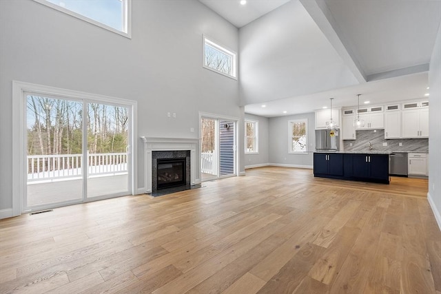 unfurnished living room with a high end fireplace, light hardwood / wood-style floors, and a healthy amount of sunlight