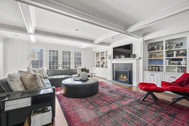 living room featuring beamed ceiling, coffered ceiling, built in shelves, and french doors