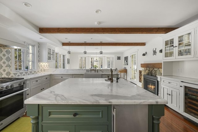 kitchen featuring stainless steel range with gas cooktop, a kitchen island, beverage cooler, light stone countertops, and white cabinets