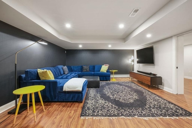 living room featuring a raised ceiling, a baseboard radiator, and light hardwood / wood-style flooring