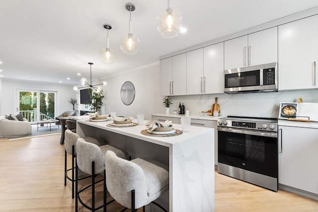 kitchen with hanging light fixtures, stainless steel appliances, white cabinets, and light wood-type flooring