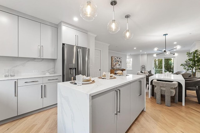 kitchen with stainless steel refrigerator with ice dispenser, tasteful backsplash, a center island, hanging light fixtures, and light hardwood / wood-style floors