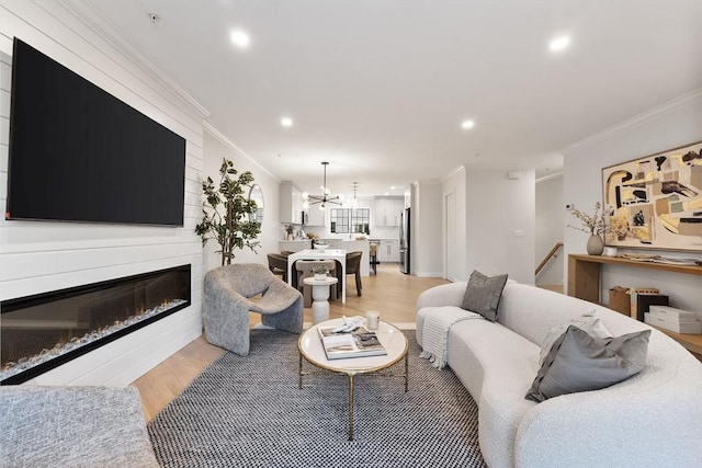 living room featuring light hardwood / wood-style floors, ornamental molding, a large fireplace, and a chandelier