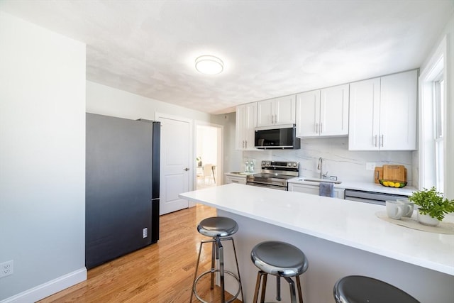 kitchen with stainless steel appliances, white cabinetry, a sink, and a kitchen bar