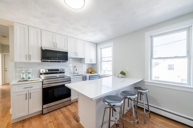 kitchen featuring a breakfast bar area, white cabinetry, light countertops, baseboard heating, and stainless steel electric range oven