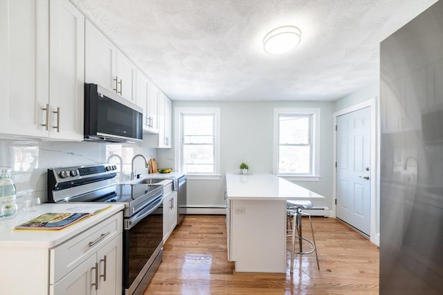 kitchen with light wood-style floors, stainless steel appliances, light countertops, and a kitchen breakfast bar