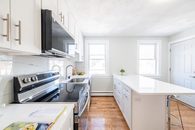 kitchen featuring light wood finished floors, stainless steel appliances, a sink, a peninsula, and a kitchen breakfast bar