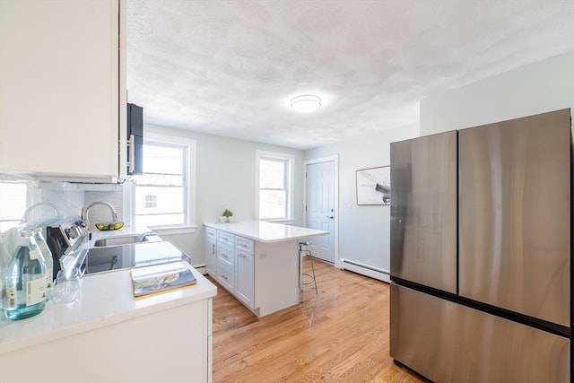 kitchen with light countertops, light wood-style flooring, freestanding refrigerator, white cabinetry, and a kitchen bar